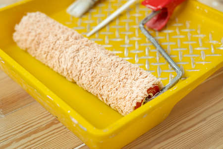 Yellow painting tray cuvette and paint roller with red handle, made of synthetic fiber.の写真素材