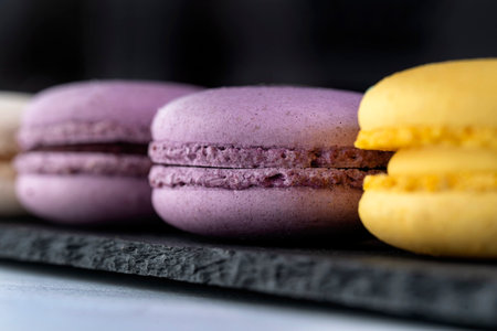 Macarons are laid out on a black slate in beautifully colored rows.の写真素材