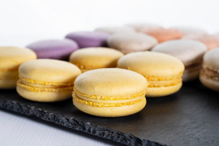 Macarons are laid out on a black slate in beautifully colored rows.の写真素材
