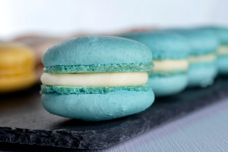 Macarons are laid out on a black slate in beautifully colored rows.の写真素材