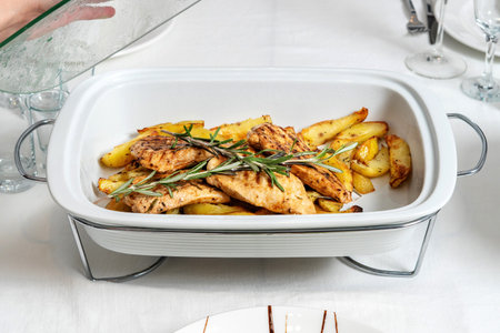 Chicken with roasted potatoes, laid out on a white platter. Decorated with rosemary.の写真素材