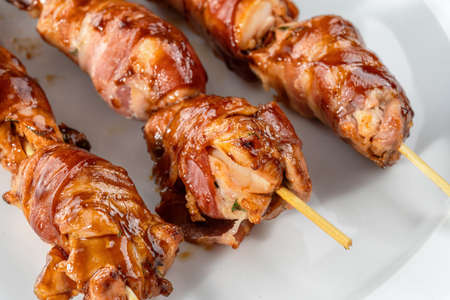 Grilled bacon-wrapped chicken tenders are laid out on a white plate. Strung on wooden skewers.の写真素材