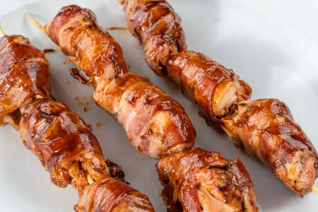 Grilled bacon-wrapped chicken tenders are laid out on a white plate. Strung on wooden skewers.の写真素材