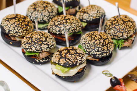 A plate of mini burgers, black rolls sprinkled with white sesame seeds.の写真素材