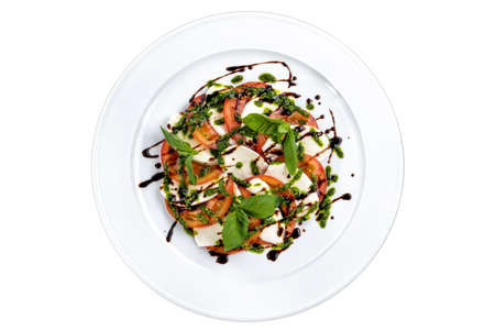 Slices of mozzarella and tomato, with fresh basil and capers sauce.の写真素材