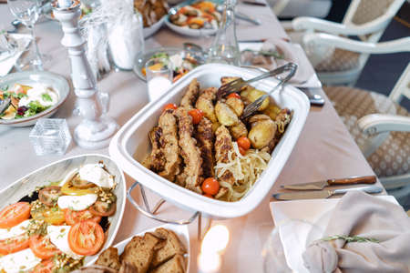 Meat with potatoes and onions, in a white food warmer. Beautiful festive table.の写真素材
