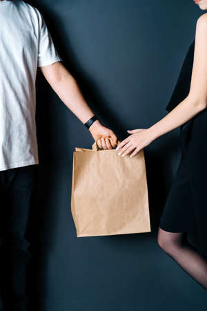 Disposable bag of kraft paper. Food delivery, hand-to-hand package transfer. The guy passes the package to the girl.の写真素材