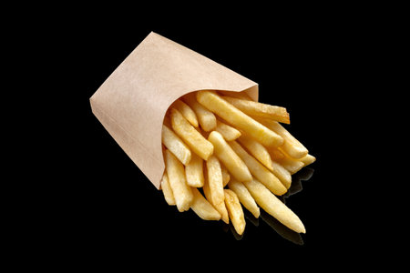 Potatoes fries in a little paper bag on a black mirrored background.の写真素材