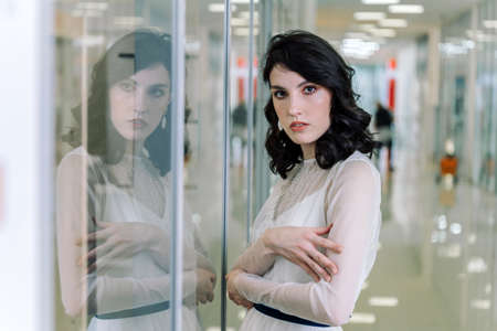 Brunette girl wearing white designer dress is reflected in the glass showcase. Look directly into the camera.の写真素材
