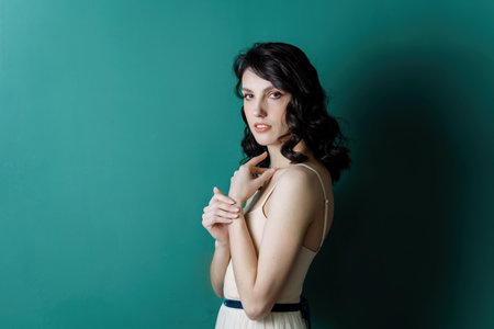 Elegant lady portrait.Pearls jewelry set posing isolated on studio green background. Stands with his shoulder to the camera.の写真素材