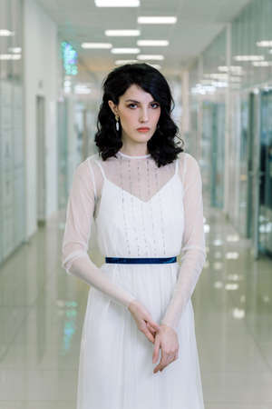 Brunette girl wearing white designer dress beautiful portrait. Vertical photo in full growth. Sad look.の写真素材