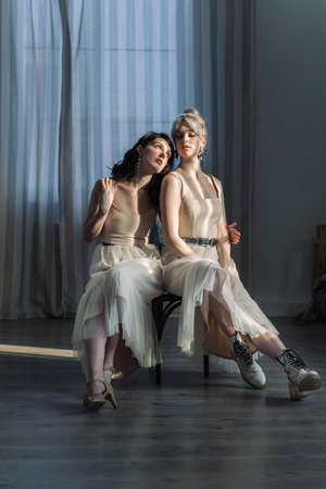 Studio portrait blondes and brunettes, looking at camera. Blue eyes, young and tender. Leaning against each other.の写真素材