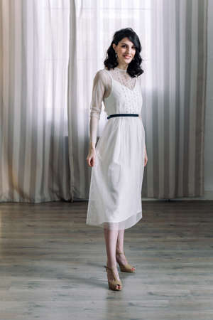 Cute young girl stands in the studio on the background of curtains. Looks at the camera and smiles. Full-length portrait.の写真素材