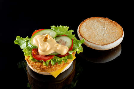 Burger with chicken cutlet, salad and mayonnaise. On a black mirrored background.の写真素材