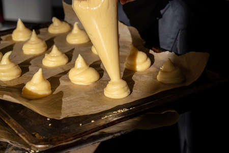 Piping choux dough for profiteroles on baking paper, beautiful sunshine.
