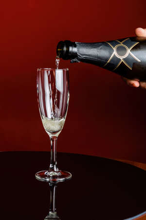 Glass of champagne against a red background, the drink is poured from a bottle.の写真素材