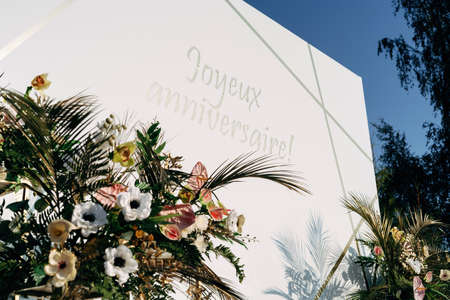 Floral photozone on party celebration, made of white plastic. Against the background of green...