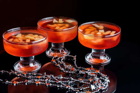 Orange jelly on a beautiful bowl with fruit pieces inside. Black background, three vases with jelly.の写真素材