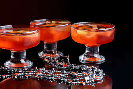 Orange jello on a beautiful bowl with fruit pieces inside. Black background, three vases with jelly. Side view.の写真素材