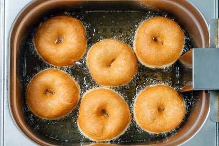 Donuts frying in deep fat. Preparation of traditional donuts, six round donuts in boiling oil.の写真素材