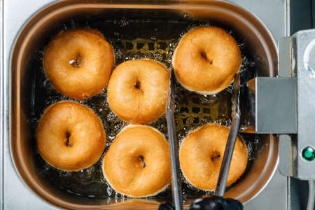 Donuts frying in deep fat. Preparation of traditional donuts, six round donuts in boiling oil.の写真素材