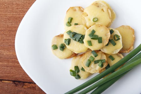 Appetizer of potatoes, cheese and green onions on wooden background. There is room for textの写真素材