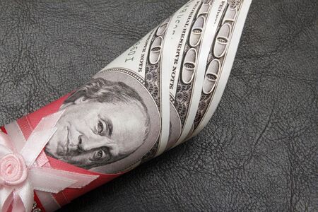 A hundred dollars in a roll on a black background, close-up. There is a place for text