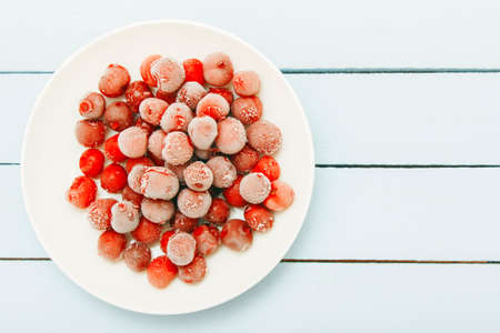 Natural medicament from colds on winter. Fresh frozen cherry on white plate. Copy space.の写真素材