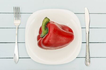 Ripe bell pepper on white plate with cutlery. Top view on wooden table. Vegetarian food concept.