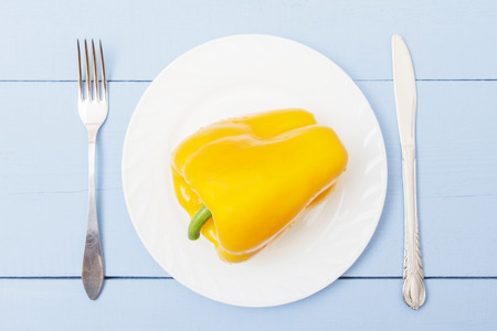 White plate, fork and knife on wooden table. Fresh colorful bell pepper on plate. Healthy food in rustic lifestyle.の写真素材
