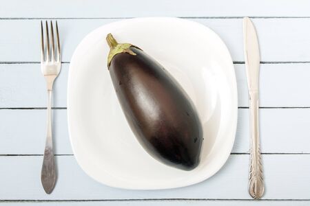 Ripe eggplant on white plate with cutlery. Top view on wooden table. Vegetarian food concept.の写真素材