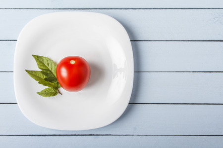 Fresh organic tomato and tomato leaves on white plate. Top view on blue wooden table with copy space. Healthy food concept.の写真素材