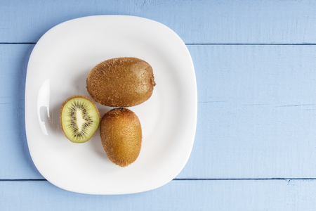 Matured kiwi fruits on white plate and on wooden table for vegetarian food. Top view. Copy space.の写真素材