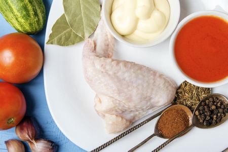 Raw meat of homemade chicken with moyonnaise and tomato sauce on white plate. Raw natural ingredients for cooking healthy food. Aromatic spices on silver spoons. Top view.の写真素材