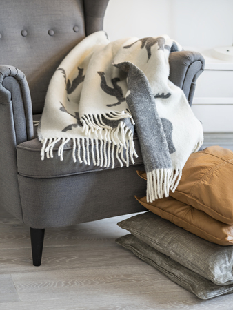 Comfortable gray armchair with warm blanket standing near pile of nice pillows in cozy room.の写真素材
