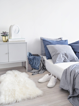 Interior shot of simple design of modern bedroom with blue and gray linen of bed and clothes in mess around.の写真素材