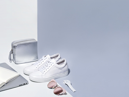 White sneakers watch sunglasses laptop open notebook and silver purse on white and gray background.の写真素材