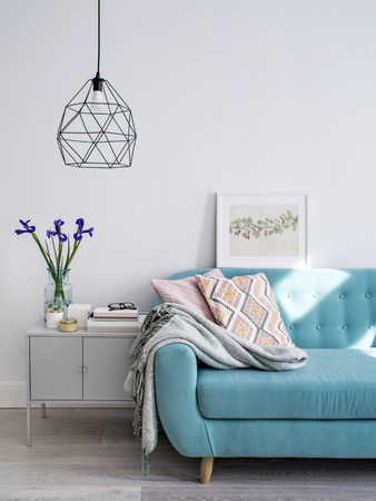 Living room with turquoise sofa and cushions in pink tones, stylish lamp, cabinet decorated with flowers and candles. Day light. Concept of modern lifestyle.の写真素材