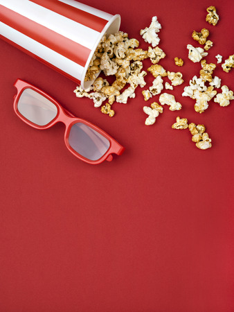 Cinema concept of red 3D glasses near snacks scattering from bucket on vinous background.の写真素材