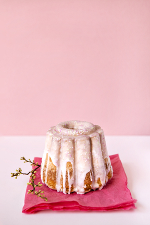 Beautiful small cake in pink glaze composed on pink napkin with small blooming branch for Easter...