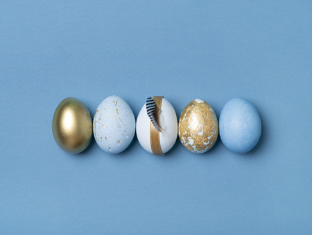 From above blue and gold decorated eggs with feather on blue background.