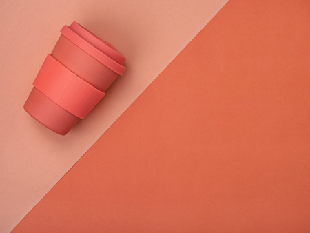 Top view of paper coffee cup in trendy coral color composed on bi colored backdrop.