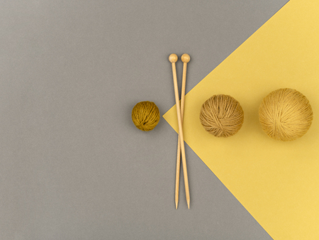 From above wooden needles placed near balls of soft natural yarn on gray and yellow background.