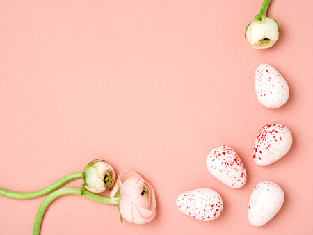 Elegant minimalist Easter Holiday frame. Red and white eggs near tender pink ranunculuses on peach pink background. Top view, space for text. Horizontal image.の写真素材