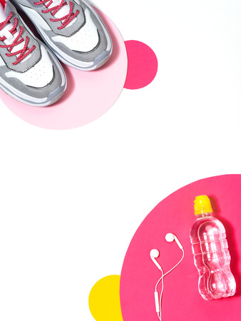 Reducing weight, getting fit and healthy life concept. Top view of white, gray and fuchsia sport shoes, bottle of water and earphones on huge confetti random size and color.の写真素材