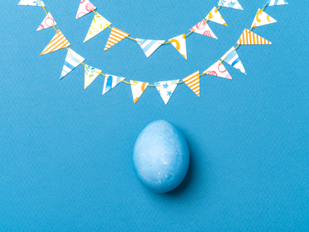 Top view of paper garland and single hand dyed blue egg decorated with golden leaves on blue background. Easter celebration concept. Horizontal image.の写真素材