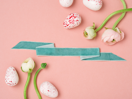 Peach pink Easter background with eggs and flowers. White and red spotted eggs accompanied with pale pink ranunculuses are separated by mint ribbon in the middle. Top view, space for text.の写真素材
