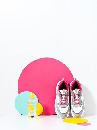Bright lit scene with bottle of water, chunky sneakers and huge confetti. Colorful casual wear or footwear.の写真素材
