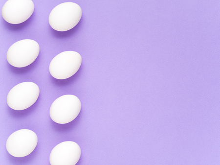 Two vertical rows of white eggs on the lavender toned paper background. Easter Holiday concept. Top view, space for text.の写真素材