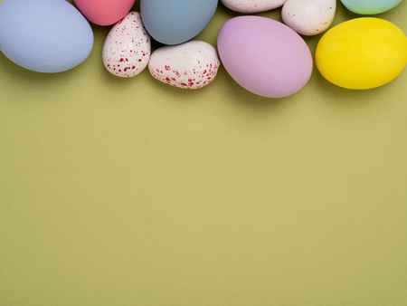 Colorful Easter eggs and treats framing. Easter Holiday background with lilac, yellow, blue and pink eggs, white and red spotted egg shaped candies. Top view, space for text.の写真素材